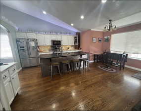 Kitchen with stainless steel appliances, white cabinetry, vaulted ceiling, and a kitchen breakfast bar.