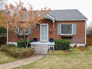 View of front of home featuring brick siding, fence, a front lawn, and roof with shingles