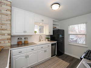 Kitchen featuring tasteful backsplash, stainless steel dishwasher, freestanding refrigerator, white cabinets, and a sink