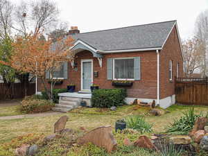 Bungalow-style house featuring brick siding, a shingled roof, fence, a front lawn, and a chimney