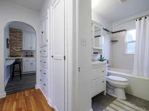 Bathroom featuring toilet, wood finished floors, vanity, decorative backsplash, and shower / tub combo with curtain