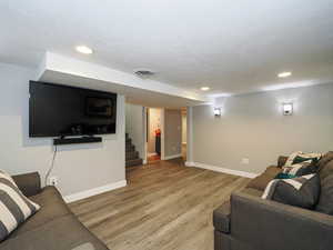 Living area featuring visible vents, a textured ceiling, light wood-style flooring, and baseboards