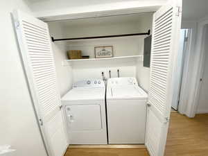 Washroom with laundry area, washing machine and clothes dryer, light wood-style flooring, and electric panel