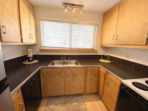 Kitchen with light wood finished floors, white electric stove, dishwasher, dark countertops, and a sink