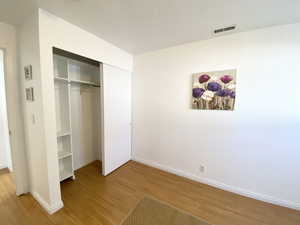 Unfurnished bedroom with light wood-type flooring, a closet, visible vents, and baseboards