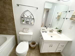 Bathroom featuring a tub to relax in, baseboards, vanity, and toilet