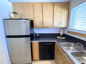 Kitchen with a sink, black dishwasher, freestanding refrigerator, light brown cabinetry, and dark countertops