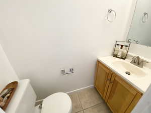 Half bath with baseboards, vanity, toilet, and tile patterned floors