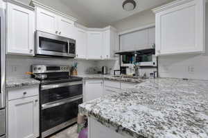 Kitchen with white cabinets, tasteful backsplash, vaulted ceiling, and stainless steel appliances