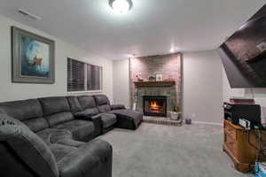 Living room featuring baseboards, visible vents, a textured ceiling, carpet floors, and a fireplace