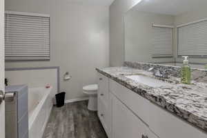 Full bathroom with baseboards, toilet, wood finished floors, vanity, and a bath