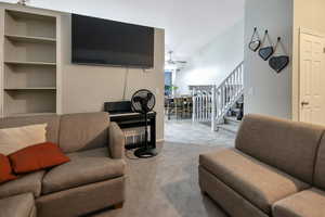 Carpeted living area featuring built in shelves, ceiling fan, and stairway