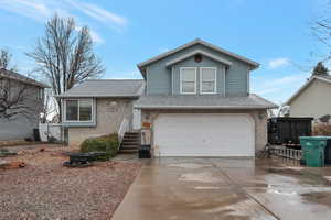 Tri-level home with a garage, a shingled roof, a fire pit, concrete driveway, and brick siding