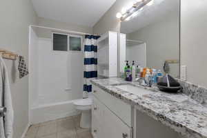 Bathroom with vanity, shower / bath combo, tile patterned flooring, and toilet