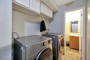 Washroom with cabinet space, washing machine and dryer, and stone finish flooring