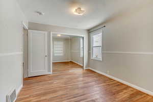 Unfurnished bedroom featuring light wood finished floors, baseboards, visible vents, and a closet