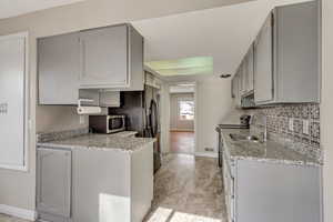Kitchen featuring appliances with stainless steel finishes, decorative backsplash, a sink, and gray cabinetry