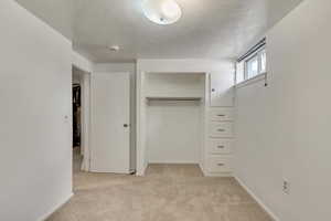 Unfurnished bedroom featuring light carpet, a textured ceiling, a closet, and baseboards