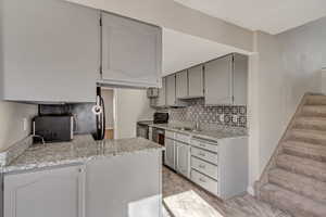 Kitchen with light stone counters, backsplash, gray cabinetry, a sink, and black / electric stove