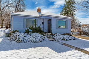 Bungalow featuring central AC unit, a chimney, and a shingled roof