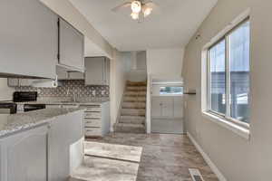Kitchen with visible vents, decorative backsplash, gray cabinetry, black appliances, and baseboards