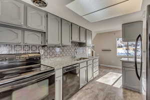 Kitchen with gray cabinetry, a sink, baseboards, decorative backsplash, and black appliances