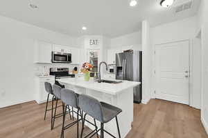 Kitchen featuring a breakfast bar area, stainless steel appliances, visible vents, a kitchen island with sink, and a sink