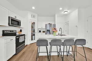 Kitchen featuring a breakfast bar area, stainless steel appliances, white cabinetry, light countertops, and light wood-type flooring