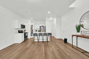 Kitchen with a breakfast bar, stainless steel appliances, light wood-style flooring, white cabinetry, and a kitchen island with sink