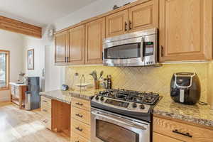 Kitchen featuring beamed ceiling, tasteful backsplash, stainless steel appliances, light wood finished floors, and light countertops