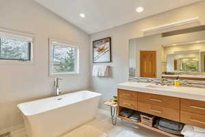 Bathroom with vanity, a freestanding tub, recessed lighting, decorative backsplash, and vaulted ceiling