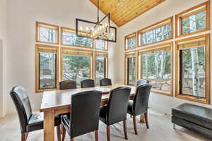 Dining area featuring baseboards, carpet flooring, wooden ceiling, a notable chandelier, and high vaulted ceiling