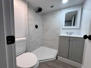 Full bath with a stall shower, visible vents, toilet, wood finished floors, and vanity