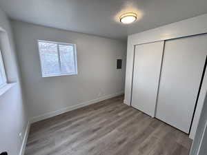 Unfurnished bedroom with electric panel, baseboards, wood finished floors, a textured ceiling, and a closet