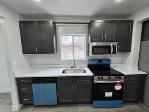 Kitchen with baseboards, appliances with stainless steel finishes, light countertops, a textured ceiling, and a sink