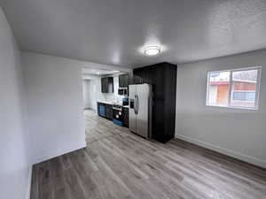 Kitchen with appliances with stainless steel finishes, light wood-type flooring, dark cabinets, and baseboards