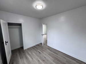 Unfurnished bedroom featuring a textured ceiling, a closet, baseboards, and wood finished floors