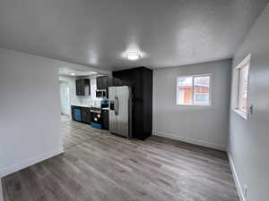 Kitchen with light wood finished floors, stainless steel appliances, a sink, dark cabinetry, and baseboards