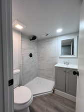 Bathroom with visible vents, toilet, a tile shower, vanity, and wood finished floors