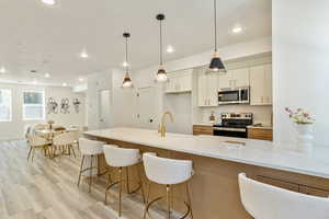 Kitchen with light stone counters, recessed lighting, a kitchen breakfast bar, appliances with stainless steel finishes, and light wood-type flooring