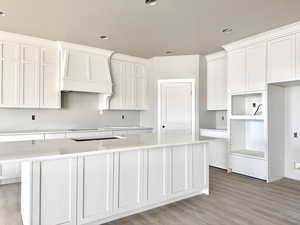 Kitchen featuring white cabinets, a center island, a textured ceiling, light wood-type flooring, and premium range hood