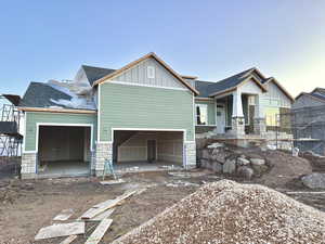 Craftsman-style house featuring an attached garage, stone siding, a shingled roof, and board and batten siding