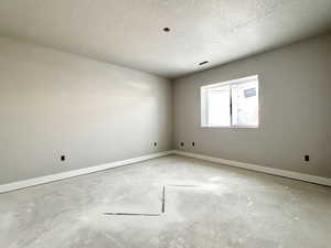 Unfurnished room with a textured ceiling, concrete floors, visible vents, and baseboards