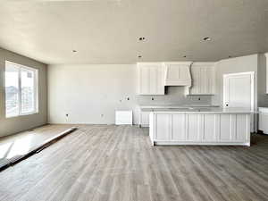 Kitchen with light wood-style floors, a kitchen island, custom exhaust hood, and white cabinets