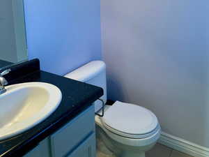 Half bath with toilet, tile patterned floors, and vanity