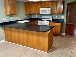 Kitchen featuring a peninsula, white appliances, dark countertops, and brown cabinets