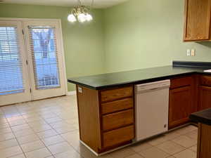 Kitchen with dark countertops, white dishwasher, a peninsula, and light tile patterned floors