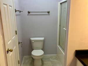 Full bathroom featuring enclosed tub / shower combo, vanity, toilet, and baseboards