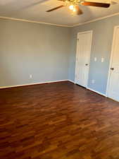 Spare room with ornamental molding, dark wood-type flooring, baseboards, and a ceiling fan