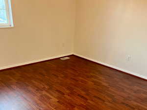 Empty room featuring dark wood-style flooring, visible vents, and baseboards